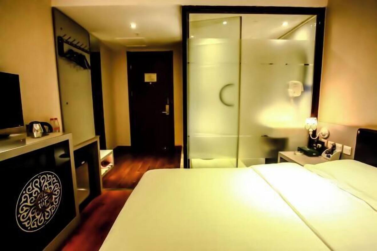 A hotel room with a bed, a desk, a chair, a TV, a mirror, and a wardrobe.