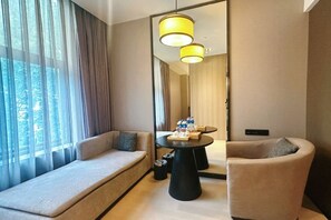 A modern hotel room with a sofa, armchair, and a round table with amenities.