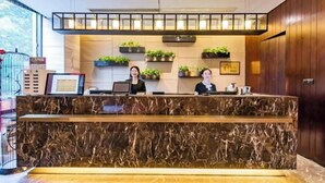 A reception desk with a marble top, two receptionists, and potted plants on shelves. - Youzhi Hotel (Hangzhou)