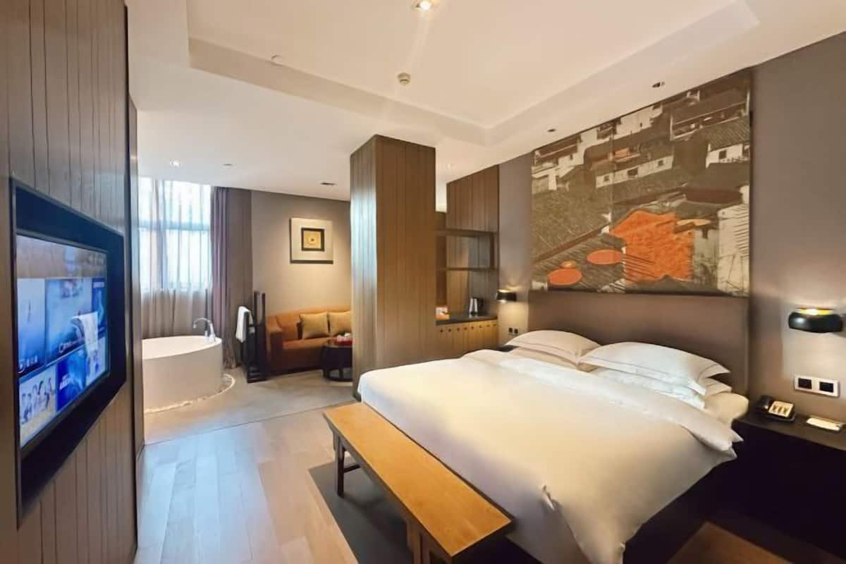 Quarto de hotel moderno com uma cama grande, um banco, uma TV, uma banheira e uma pintura da paisagem urbana na parede.