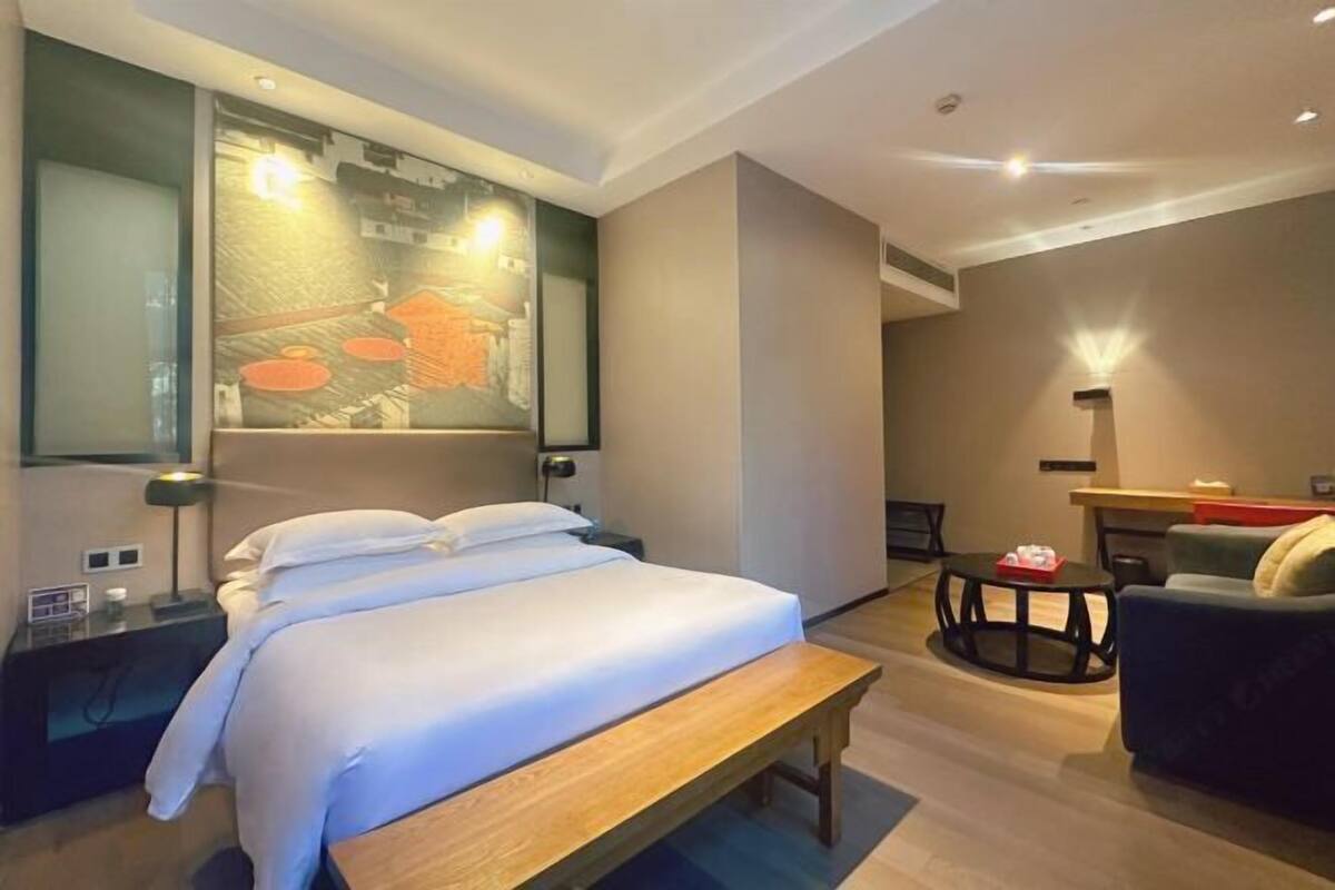 Quarto de hotel moderno com uma cama grande, um banco, uma mesa redonda e um sofá.