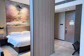 A modern hotel room with a large bed, a painting on the wall, and a wooden door.