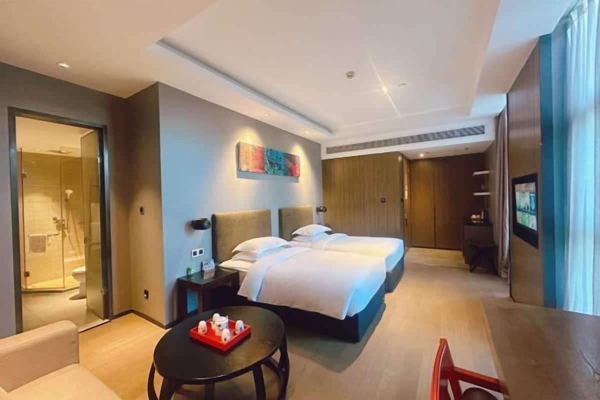 Quarto de hotel com uma cama, uma mesa com um tabuleiro de objetos, televisão e cabine de hidromassagem de vidro.