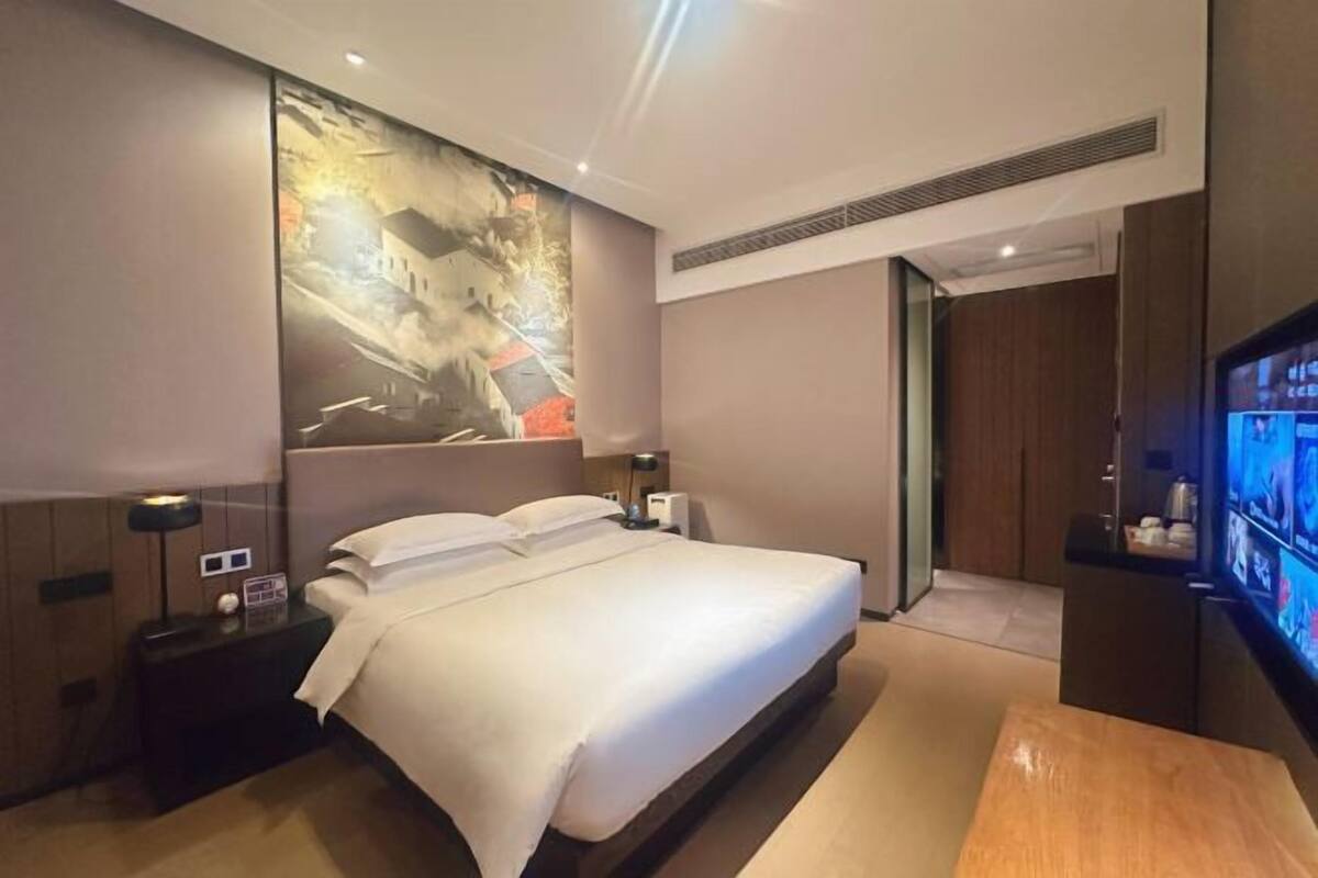 Quarto de hotel com uma cama grande, televisão, mesa de cabeceira e um quadro na parede.