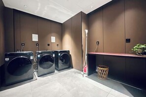 A laundry area with three washing machines, a red trash bin, and a plant on a shelf. - Youzhi Hotel (Hangzhou)