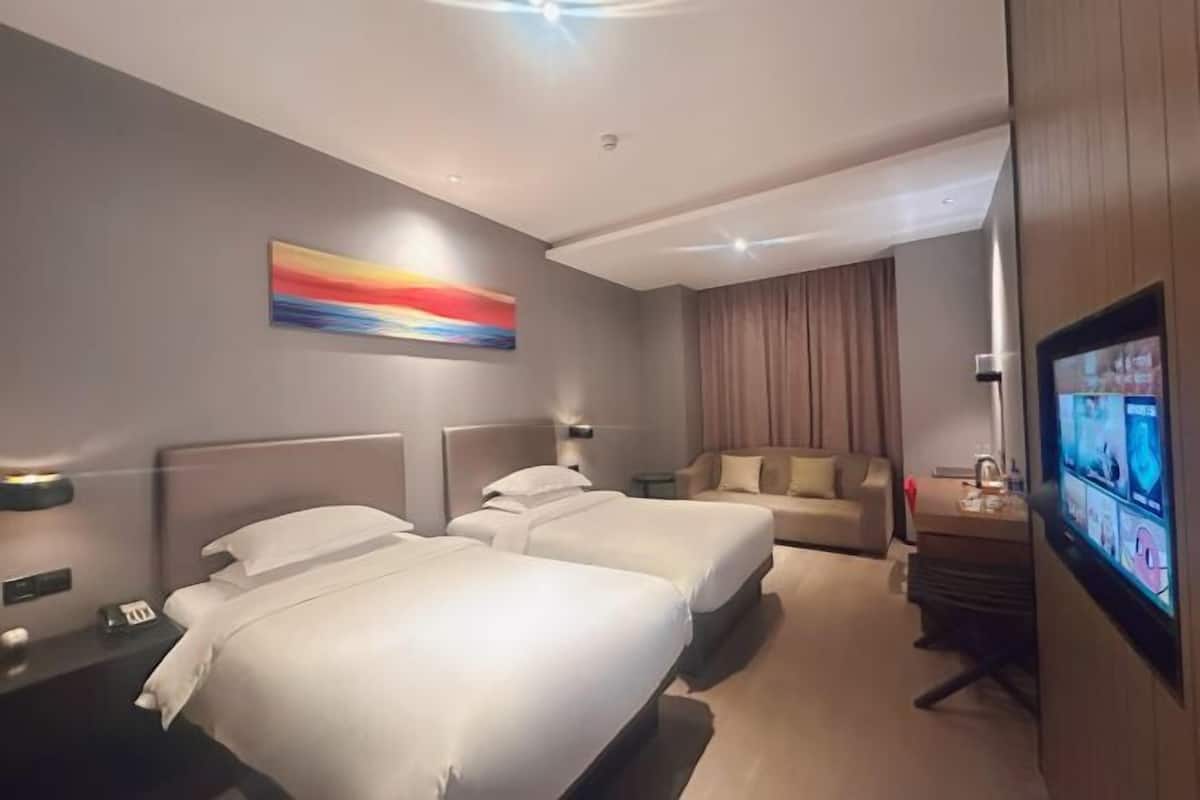 Quarto de hotel com duas camas, televisão, escrivaninha e um quadro na parede.