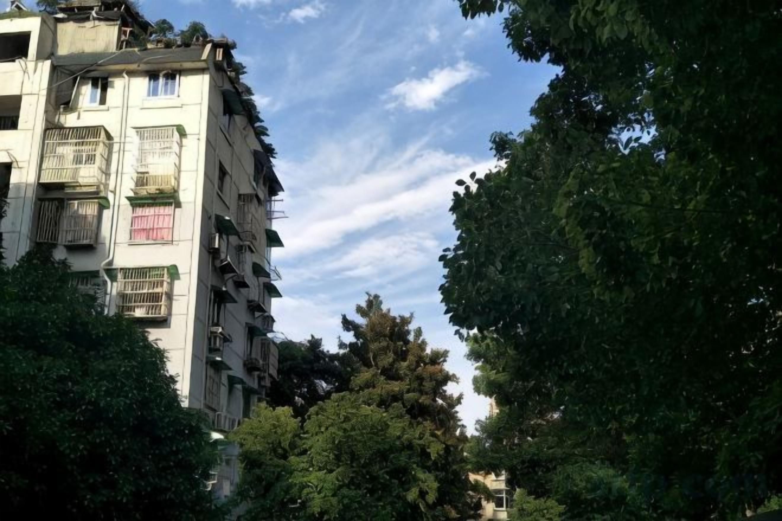 A multi-story building with balconies, surrounded by trees.