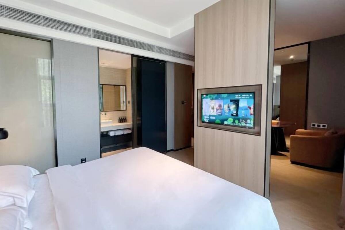 Quarto de hotel moderno com cama, televisão presa à parede, guarda-roupa e área de estar.