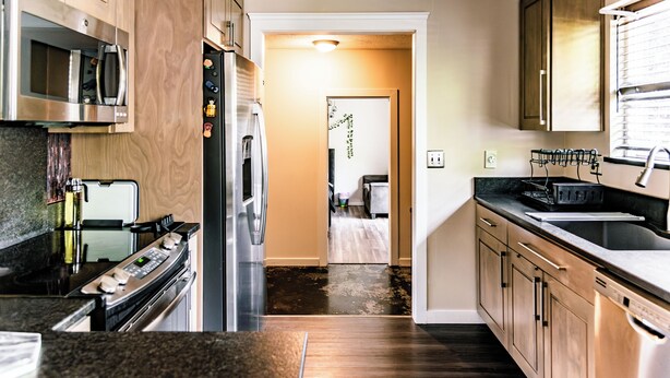 A modern kitchen with stainless steel appliances, wooden cabinets, and a dark hardwood floor. - Modern Minimalist Home 4BR 5 Beds, AC Comfort & Wifi (Burlington)