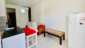 A compact kitchen with a refrigerator, a dining table with chairs, and a bench.