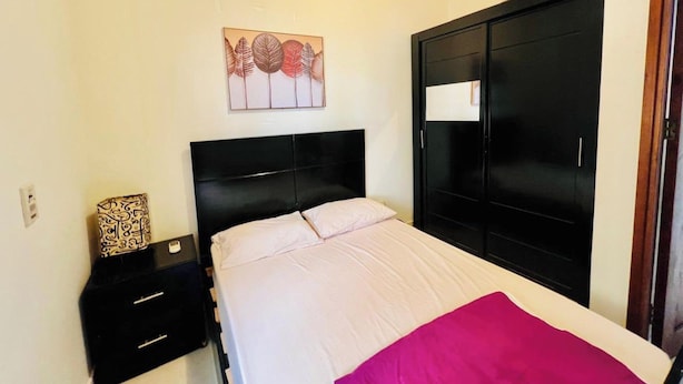 A bedroom with a bed, a nightstand, a wardrobe, and a wall-mounted artwork.