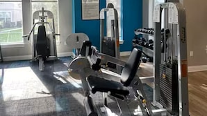 Une salle de sport équipée de divers appareils d’exercice, dotée de grandes fenêtres et d’un mur d’accent bleu.