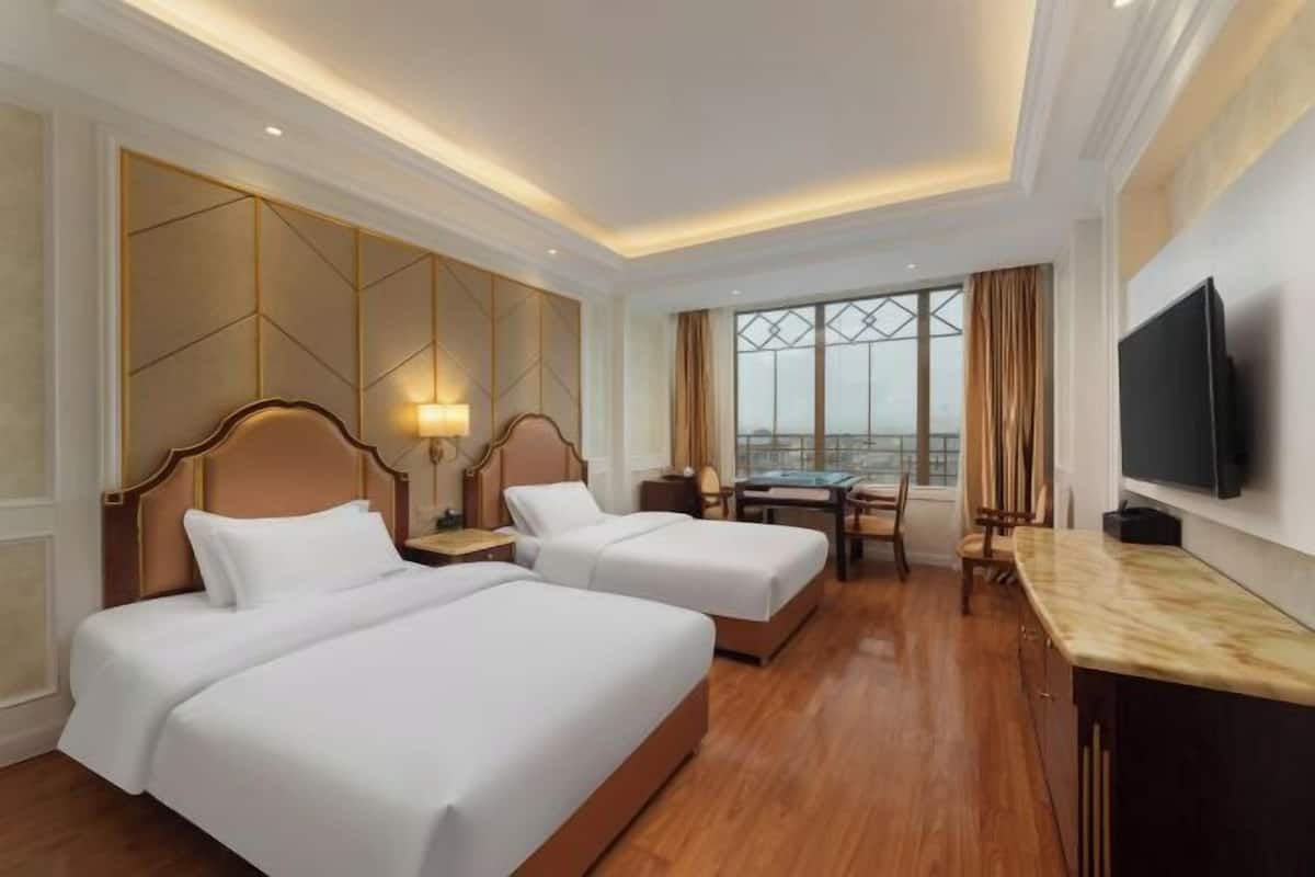 A hotel room with two beds, a desk, a TV, and a view of the city.