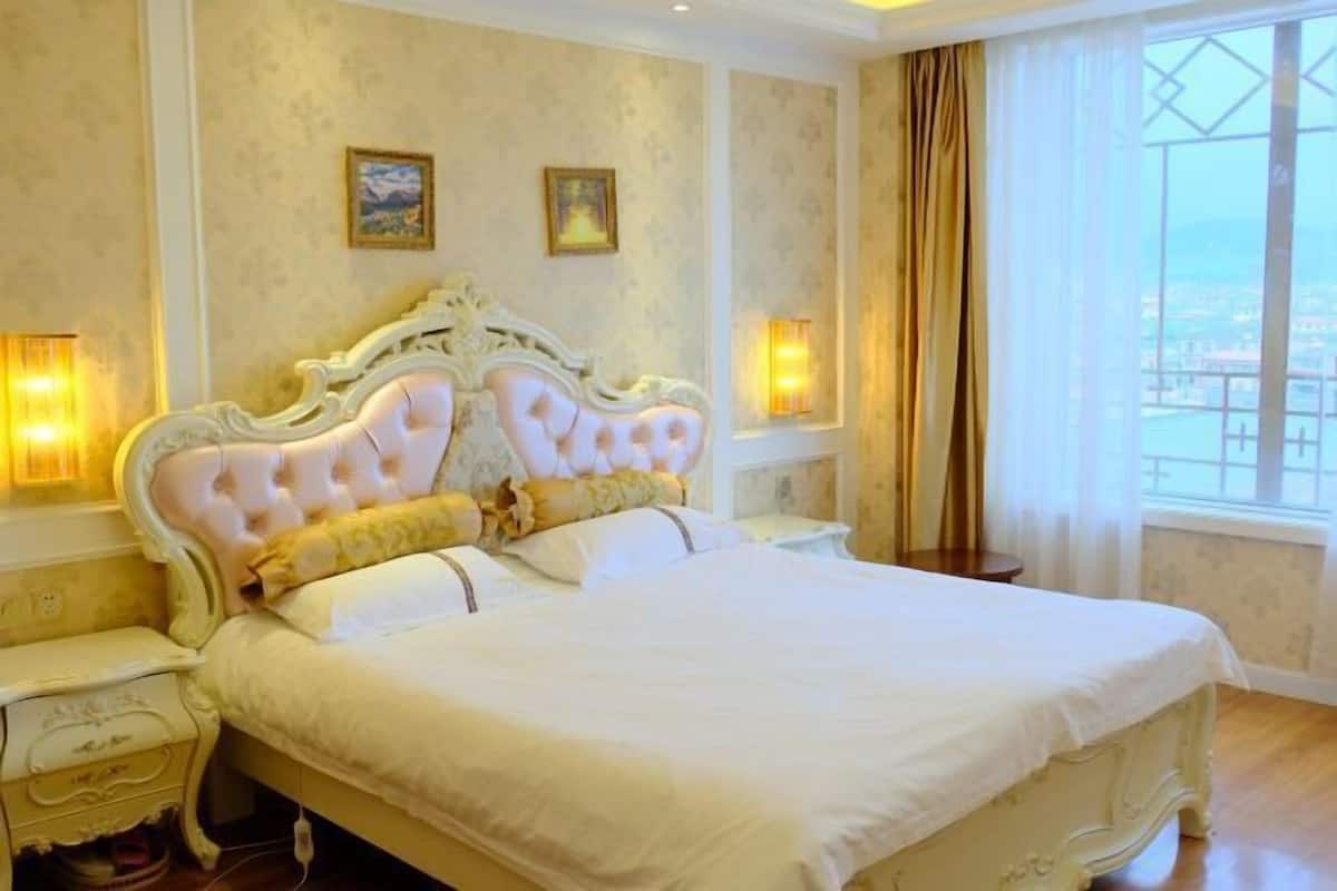 A large bed with ornate headboard, two bedside tables, and a view of the city through a window.