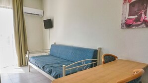 Een kamer met een bed, een tafel en een stoel. Er is een raam met gordijnen, een airconditioning en een televisie aan de muur bevestigd.