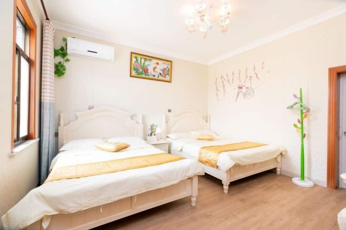 Een slaapkamer met twee bedden, een kroonluchter, een wandairconditioner en een raam met gordijnen.