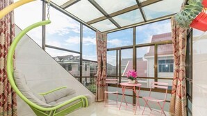 Een kamer met een glazen plafond, een groene stoel, een tafel met roze stoelen, en een raam met gordijnen.