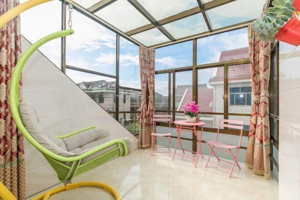 Een kamer met een glazen plafond, een groene stoel, een tafel met roze stoelen, en een raam met gordijnen.