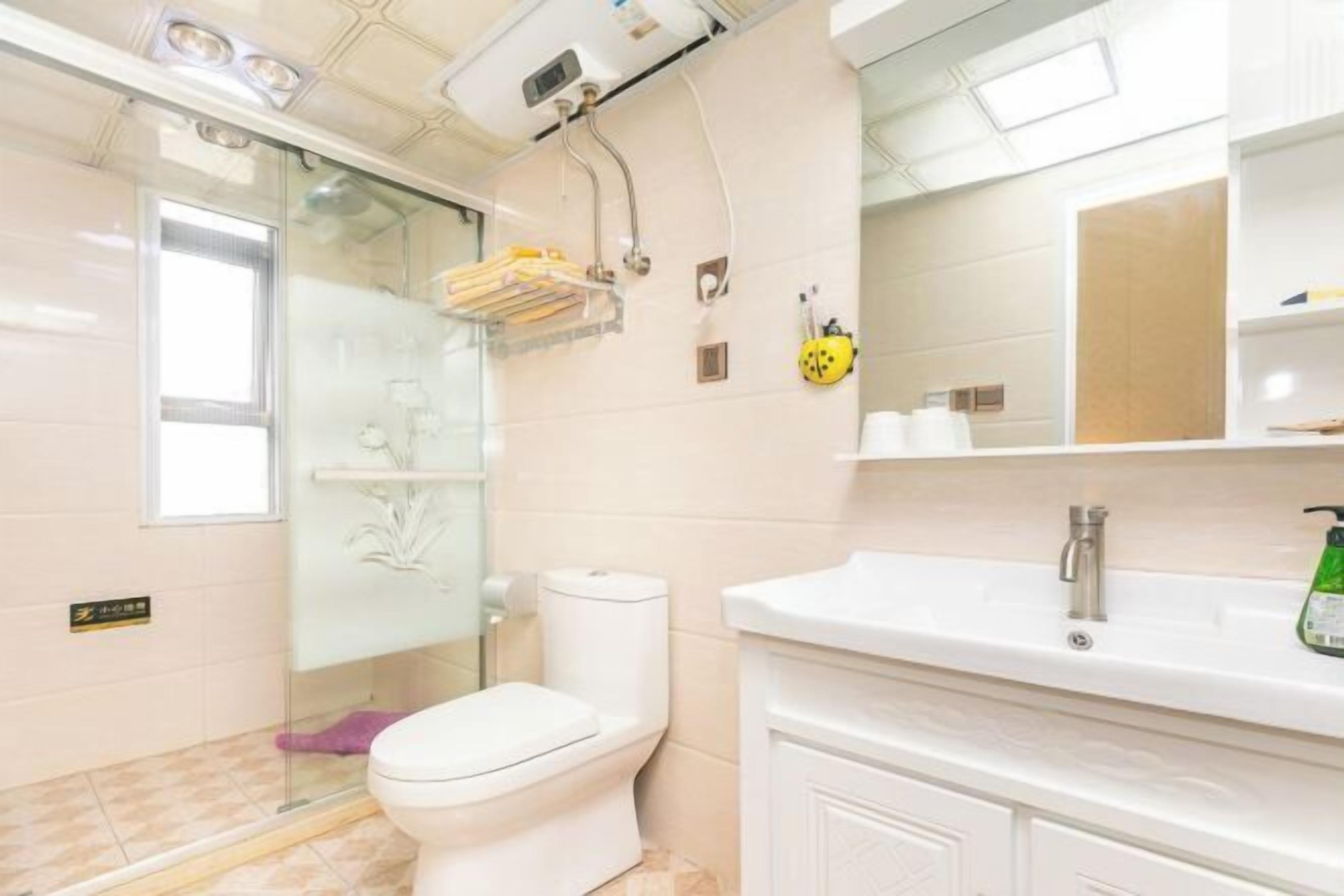 Un baño con inodoro, cabina de ducha de vidrio, lavabo con espejo y estante con artículos de aseo.