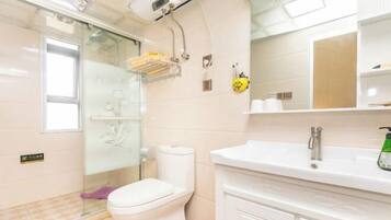 Un baño con inodoro, cabina de ducha de vidrio, lavabo con espejo y estante con artículos de aseo.