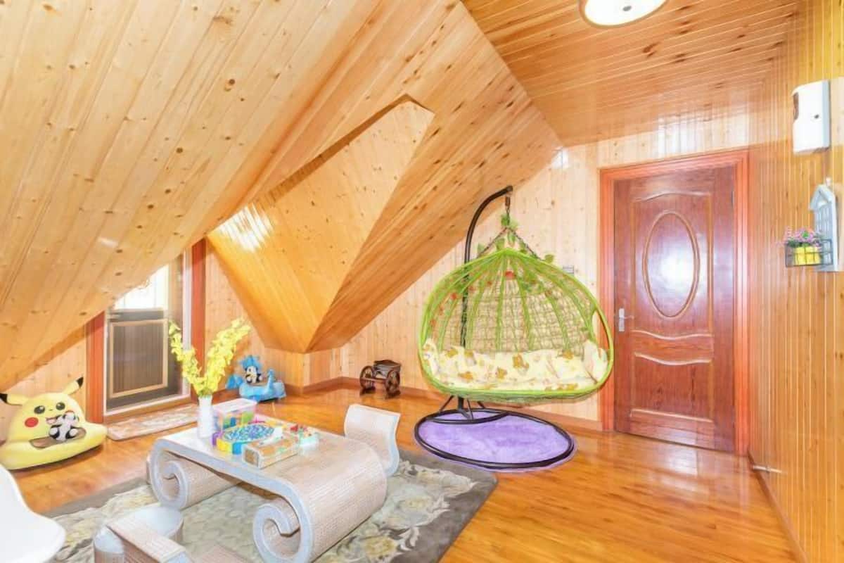 Een gezellig zolderkamer met houten wanden en een schuine kap. Er staat een groene hangstoel, een klein tafeltje met speelgoed en een deur met een decoratieve knop.