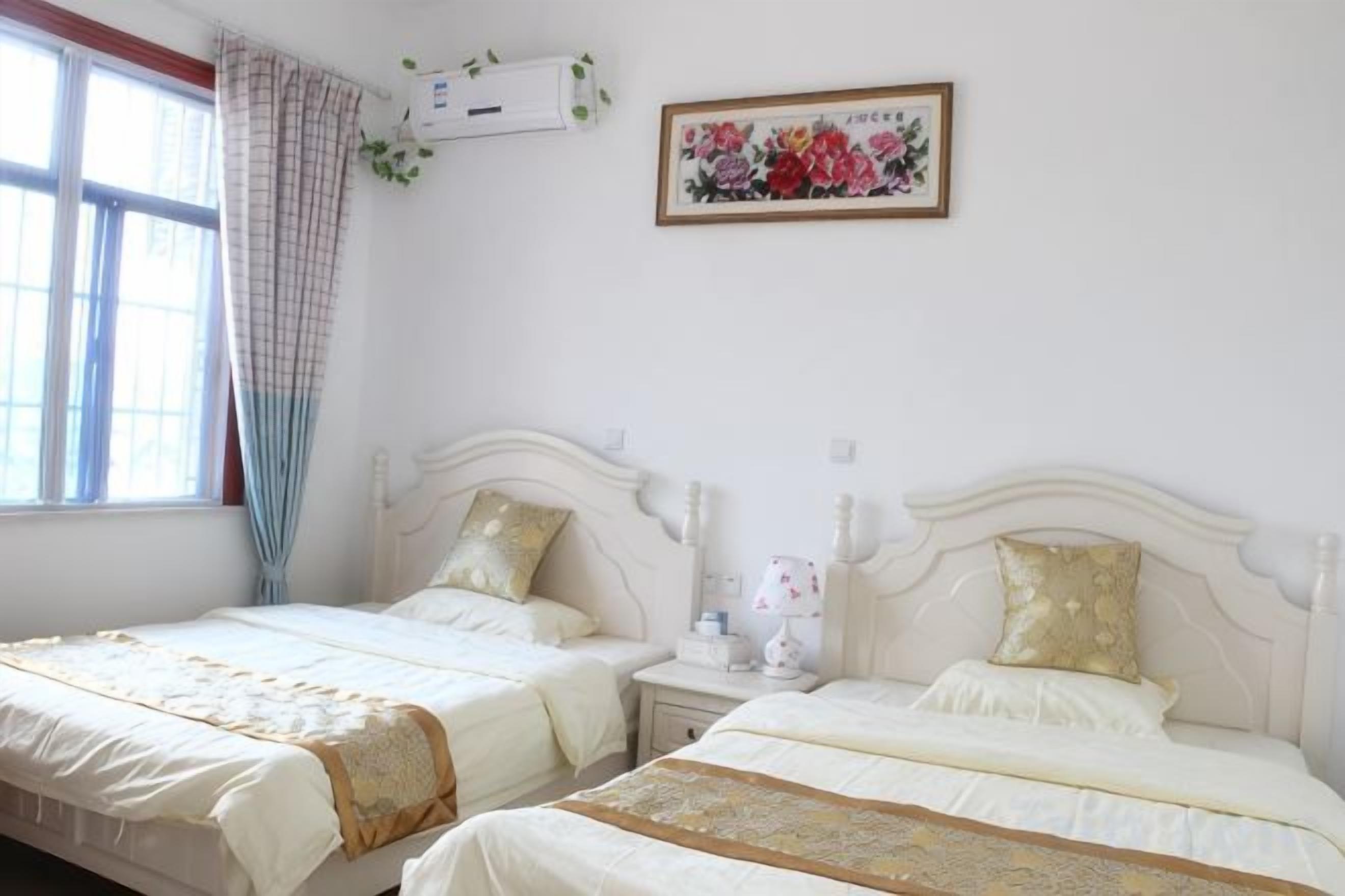 A bedroom with two beds, a window with curtains, an air conditioning unit, and a floral painting on the wall.