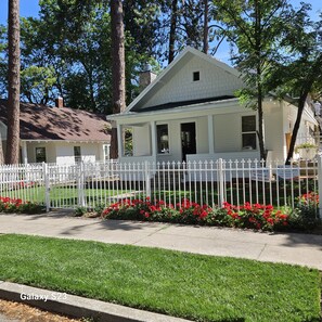 A white two-story house with a white picket fence, surrounded by red flowers and green grass. - Lake Coeur d'Alene Inn Guest House (Coeur d'Alene)