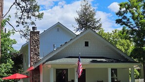 A red vintage car parked in front of a white house with a porch, a white picket fence, and an American flag. - Lake Coeur d'Alene Inn Guest House (Coeur d'Alene)