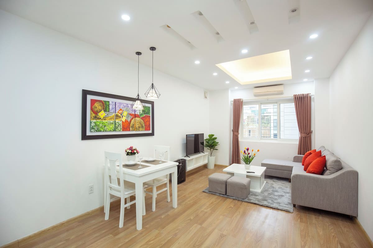 A modern living room with a dining area, a grey sofa, a TV, and a painting on the wall.