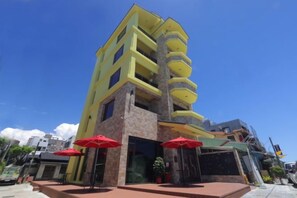 A multi-story building with a yellow facade, outdoor seating with red umbrellas, and a clear blue sky. - Nottingham Ocean Castle B&B (Hualien)