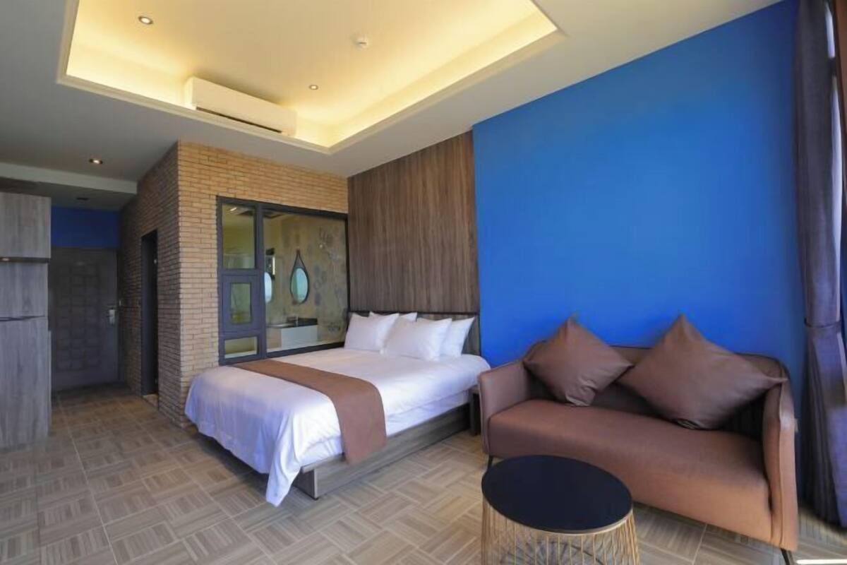 Una habitación de hotel moderna con una cama grande, un sofá, una mesita pequeña y una lámpara en el techo.