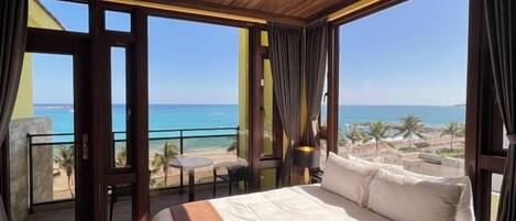 Un dormitorio con una cama grande, un balcón con vistas a la playa y una mesa con sillas.