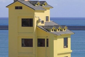 Un edificio amarillo de varios pisos con techo plano, varias ventanas y vista al océano.