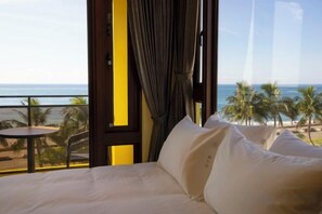 A hotel room with a bed, a view of the ocean, and a balcony with palm trees.