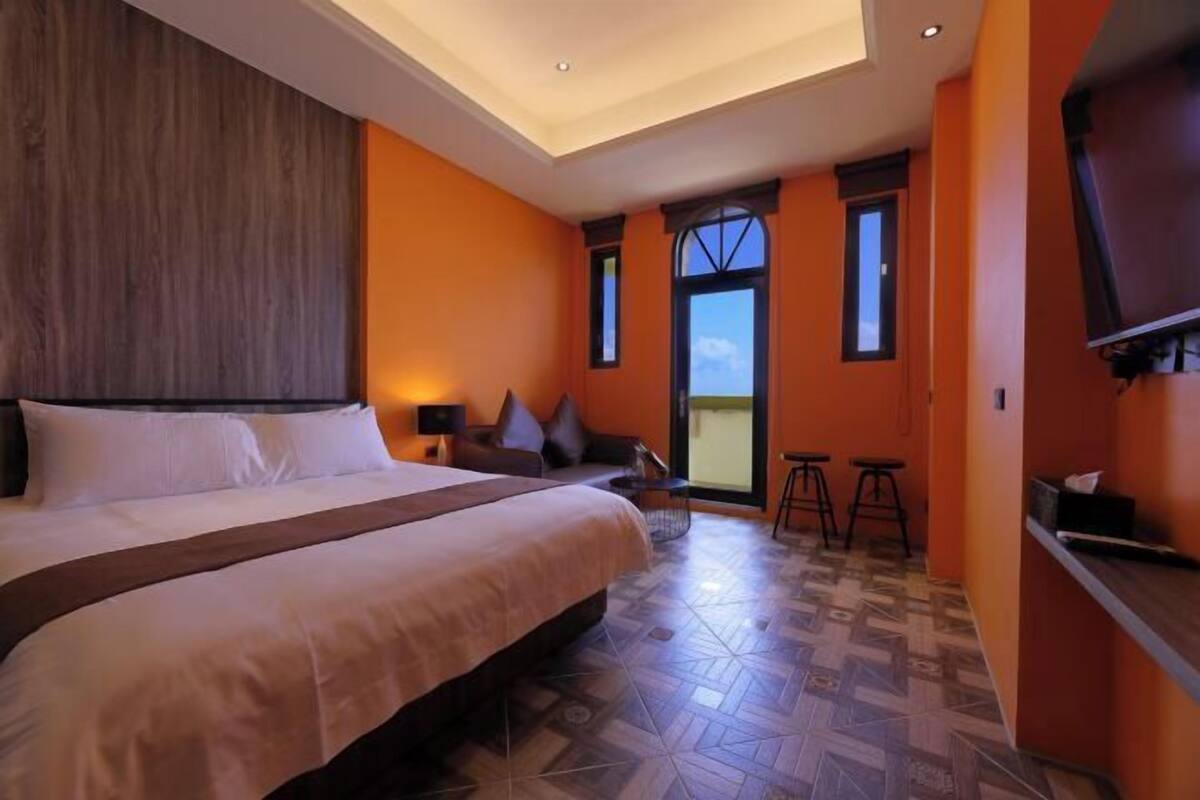 Habitación de hotel con una cama grande, un sofá, un televisor y un balcón con vistas.