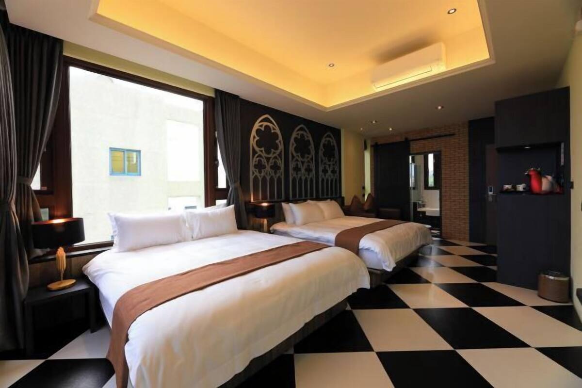 Habitación de hotel con dos camas, piso a cuadros y un ventanal con cortinas.