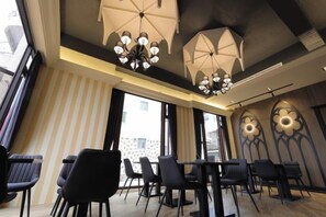 A modern interior with a dining area featuring tables and chairs, large windows, and decorative ceiling lights.