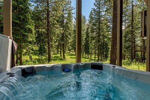 A hot tub in a forested area with tall trees and a clear sky.