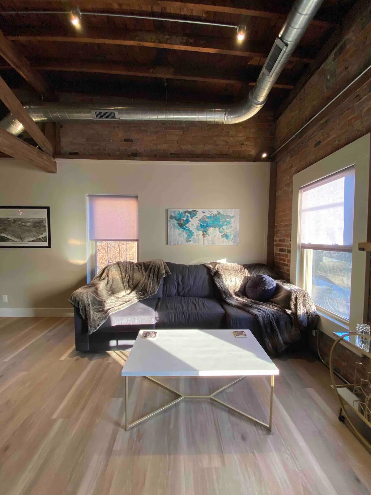 A modern living room with a dark leather sofa, a white coffee table, and a large window providing natural light.
