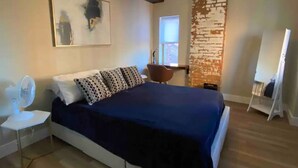Une chambre avec un grand lit, un ventilateur de plafond, un tableau au mur et un mur d’accent orné d’un motif en briques.
