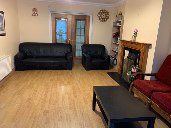 A living room with two black sofas, a red chair, a wooden coffee table, a fireplace, and a bookshelf. - Room-ensuite With King Bed 2 (Dublin)