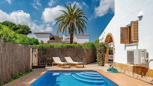 A swimming pool with two lounge chairs, a palm tree, and a white building with a tiled roof. - Cofitsa Plus by Interhome (Jávea)