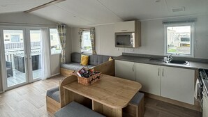 Moderni keittiö, jossa on puinen pöytä ja penkit, sisäänrakennettu mikroaaltouuni ja suuri ikkuna.