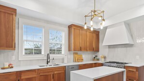 A modern kitchen with wooden cabinets, a central island, a built-in stove, and a window with blinds. - Old-Portland Charmer in the Alphabet District (Portland)