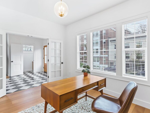 A modern office space with a wooden desk, leather chair, and large windows with blinds.