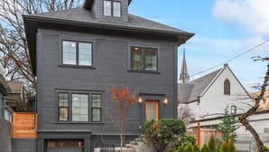 A two-story house with a gray exterior, a front garage, and a small front yard with a fence and some plants. - Old-Portland Charmer in the Alphabet District (Portland)