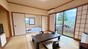 Une pièce de style japonais traditionnel, avec un sol recouvert de tatamis, une table basse avec des coussins, une porte coulissante et une vue sur un jardin, visible à travers de grandes fenêtres.