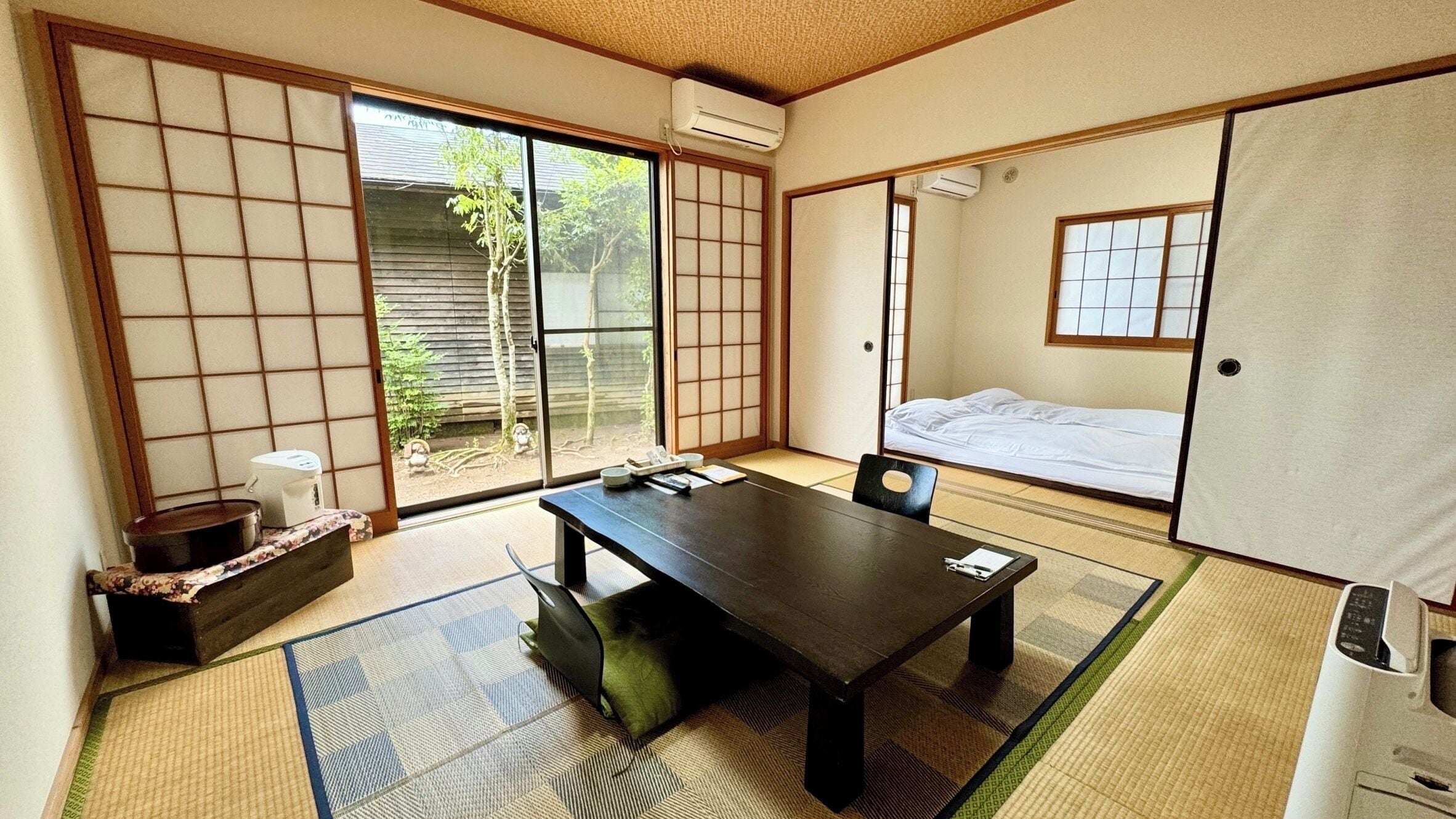 Um quarto japonês tradicional com tatames, uma porta deslizante, uma cama e uma mesa com uma cadeira.