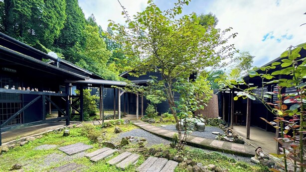 Un jardin japonais traditionnel avec des allées pavées de pierres, un petit arbre et des structures en bois.