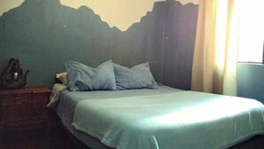 Ein Schlafzimmer mit einem Bett, Kissen, einem Nachttisch und einer Wand mit Bergmotiv.